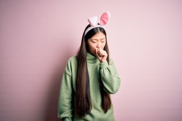 Young asian woman wearing cute easter bunny ears over pink background feeling unwell and coughing...
