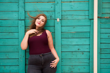 Beautiful woman wearing ripped jeans standing against cafe wall on city street. Casual fashion, elegant everyday look. Plus size model.