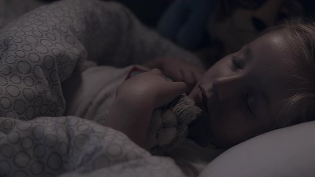 Little girl sleeps peacefully with stuff animal in bed, pan, close-up