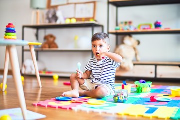 Beautiful toddler boy sitting on puzzle playing meals with plastic plates, fruits and vegetables at kindergarten