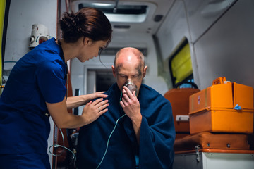 Doctor stands with man who sits in oxygen mask in blanket