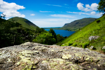 Fototapeta na wymiar A close up of a moss covered textured rock with an out of focus mountainous and lake background.