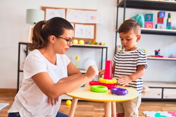 Beautiful teacher and toddler boy building pyramid with hoops bolcks at kindergarten