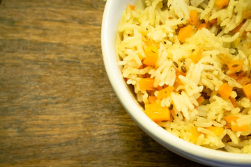 Yellow rice with curry and vegetables in white bowl on light wooden surface. Healthy balanced breakfast snack.