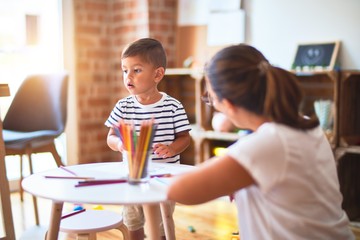 Beautiful teacher and toddler boy drawing draw using colored pencils at kindergarten