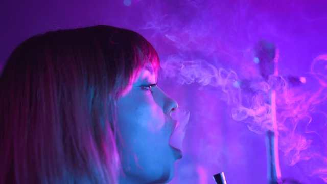 Pretty young woman enjoying hookah at the bar feel happy young friendship communicate emotion shisha smoker male lounge handsome female vape beautiful attractive company relax slow motion neon lights