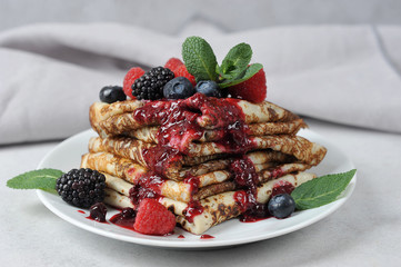 Pancakes with berry jam. Pancakes on a plate are decorated with fresh berries of raspberries, blueberries, blackberries and mint. Light background. Close-up. Macro shot.