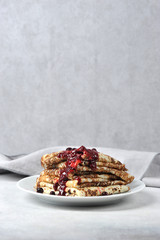 Pancakes with berry jam. A plate with pancakes is decorated with fresh berries and mint. The vertical orientation of the frame. Free space for text.