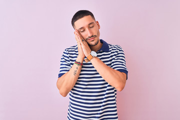 Young handsome man wearing nautical striped t-shirt over pink isolated background sleeping tired dreaming and posing with hands together while smiling with closed eyes.