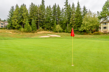 Obraz premium Golf course with gorgeous green, sand bunker and golf flag and real estate on background.