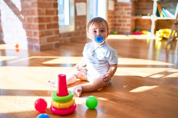 Adorable toddler sitting on the floor using pacifier around lots of toys at kindergarten