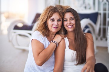 Fototapeta premium Beautiful mother and daugther sitting at terrace hugging and smiling
