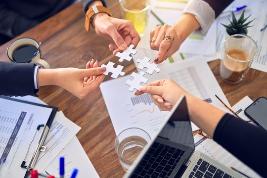 Group of business workers with hands together connecting pieces of puzzle at the office