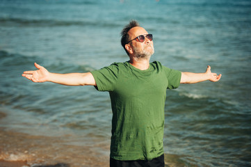 Portrait of happy middle age man enjoying nice sunny day on the beach, wearing green t-shirt and...