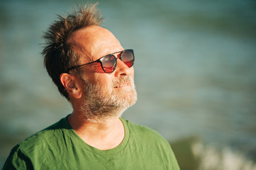 Outdoor portrait of happy middle age man enjoying nice sunny day on the beach, wearing green...