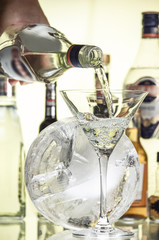 Hand with a bottle pours martini into a glass against the background of the bar