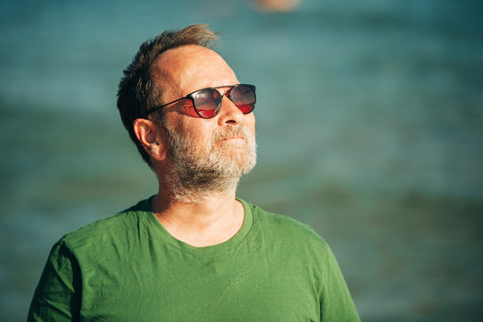 Outdoor portrait of happy middle age man enjoying nice sunny day on the beach, wearing green t-shirt and sunglasses