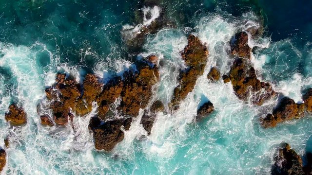 Waves are breaking on stones. Wave foaming and splashing ocean surf. Aerial top down view. Tenerife island, Spain. 4K, UHD