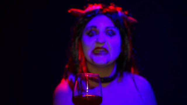 Woman devil with an ominous smile with a glass in his hand from sharpness to blur.
