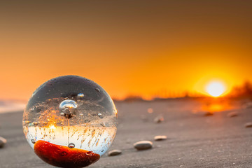 Boule de cristal sur une plage au coucher du soleil avec reflets sur le sable.