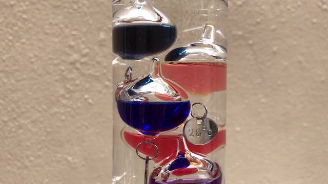 Tilting up shot of a Galileo Thermometer with six vessels with different colored liquid at the top