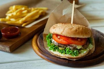 big tasty burger on a wooden table and french fries. Delicious burger with beef, tomato, cheese and lettuce.