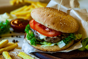 big tasty burger on a wooden table and french fries. Delicious burger with beef, tomato, cheese and lettuce.