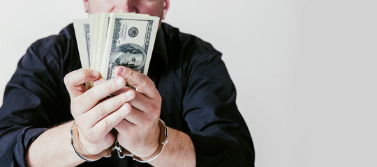 Close up businessman with tied in handcuffs hands before money as symbol of corruption, fraud and bribe.
