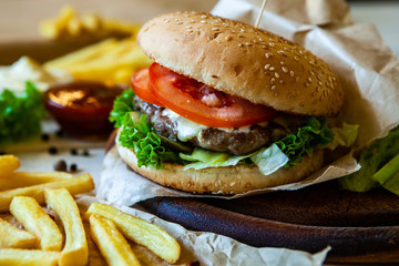 big tasty burger on a wooden table and french fries. Delicious burger with beef, tomato, cheese and lettuce.