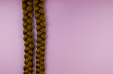 Two blond braids on a pink background, lie in parallel.