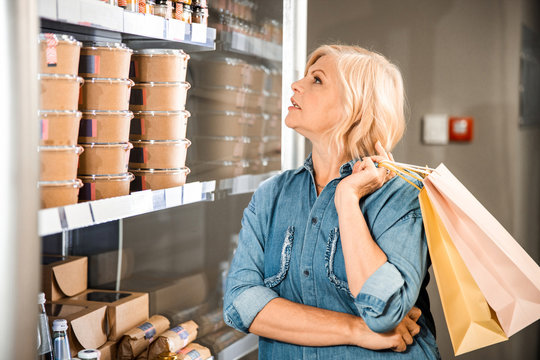 Beautiful adult woman looking on shelves with groceries in the store