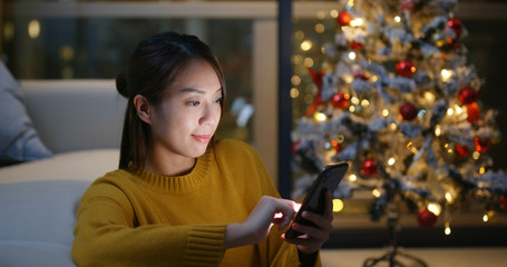 Woman use of smart phone with christmas tree decoration at home
