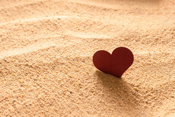 Fototapeta premium Burgundy heart in the sand in the light of backlight.