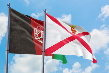 Jersey and Afghanistan flags waving in the wind against white cloudy blue sky together. Diplomacy concept, international relations.