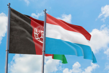 Luxembourg and Afghanistan flags waving in the wind against white cloudy blue sky together. Diplomacy concept, international relations.