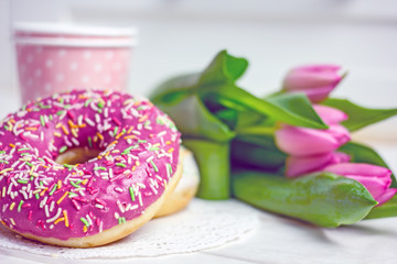 Fototapeta na wymiar Women's Day breakfast. Beautiful sweet donuts in multi-colored glaze, a cup of coffee, pink tulips on a wooden background, copy space 