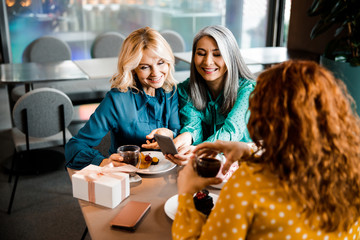 Joyful ladies using cellphone and enjoying drinks