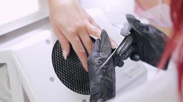 A gloved manicurist woman in a beauty salon nails a client with a nail file before applying a gel coating