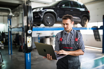 Smiling man mechanic using a laptop computer to check a car engine