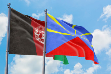 Reunion and Afghanistan flags waving in the wind against white cloudy blue sky together. Diplomacy concept, international relations.