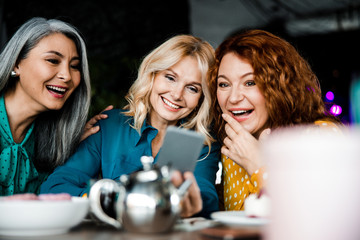 Joyful ladies watching something interesting on cellphone