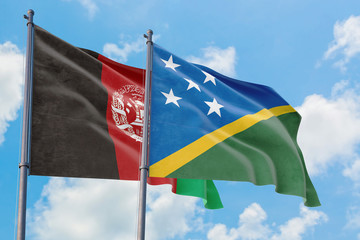 Solomon Islands and Afghanistan flags waving in the wind against white cloudy blue sky together....