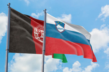 Slovenia and Afghanistan flags waving in the wind against white cloudy blue sky together. Diplomacy concept, international relations.