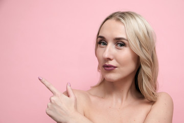 Obraz premium Beautiful blond woman with naked shoulders on pastel pink background. Beauty, cosmetics and skin care concept