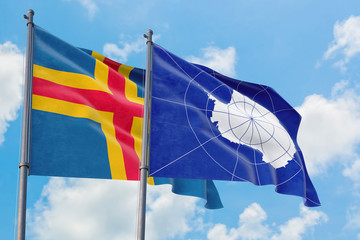 Antarctica and Aland Islands flags waving in the wind against white cloudy blue sky together. Diplomacy concept, international relations.