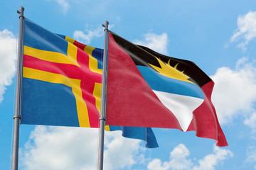 Antigua and Barbuda and Aland Islands flags waving in the wind against white cloudy blue sky together. Diplomacy concept, international relations.