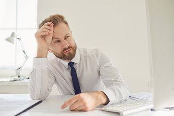 Serious busy businessman reads working documents sitting at a table with a computer in the office.