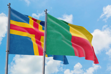 Benin and Aland Islands flags waving in the wind against white cloudy blue sky together. Diplomacy concept, international relations.
