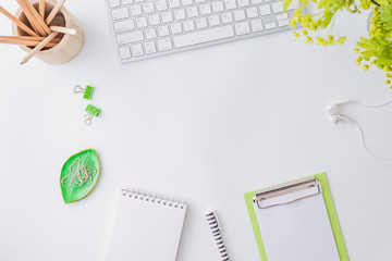 Flat lay blogger or freelancer workspace with a laptop, branches with green leaves, office supplies on a light background