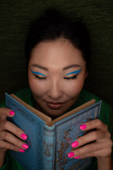 Asian girl in blue colored make up reads an old book with blue cover